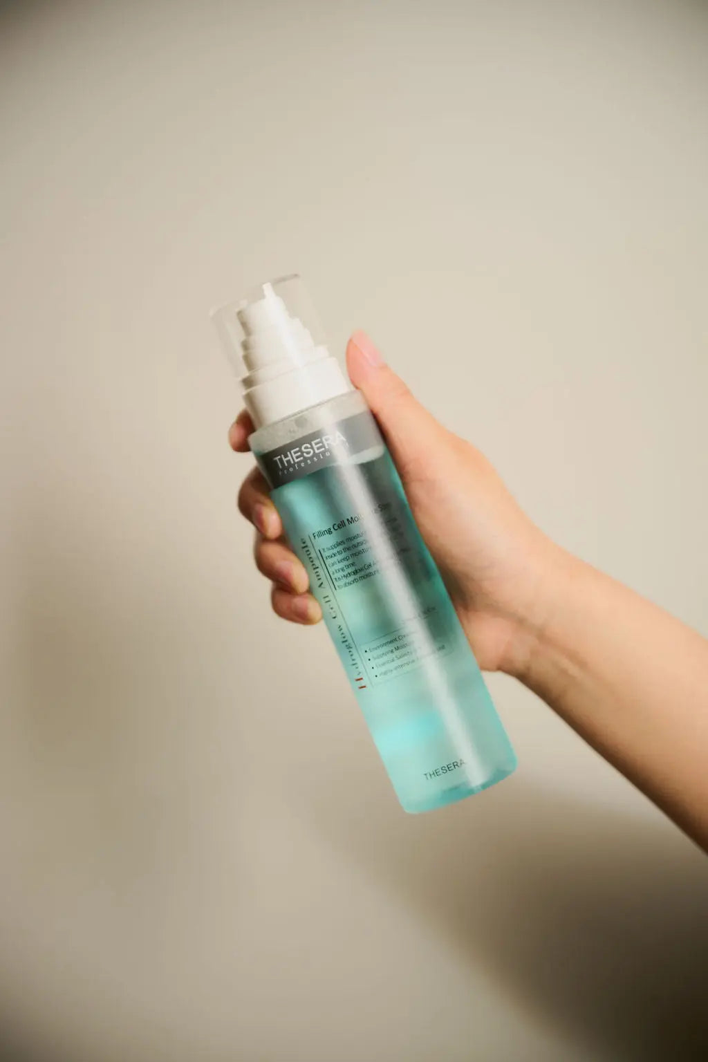Hand holding a blue spray bottle with a white nozzle against a neutral background